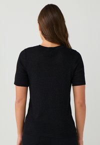 T-shirt nera a maniche corte realizzata in tessuto testurizzato, con collo rotondo e silhouette aderente, mostrata da dietro.