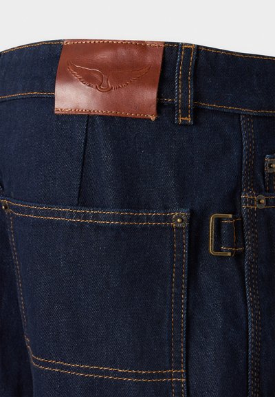 Τζιν παντελόνια σε σκούρο μπλε με ραφές σε καφέ απόχρωση. Διαθέτουν καφέ δερμάτινη ετικέτα στη μέση με ανάγλυφο λογότυπο. Περιλαμβάνουν τσέπες και μεταλλικά διακοσμητικά στοιχεία.
