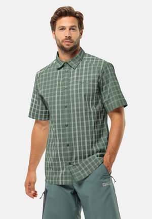 Chemise à manches courtes, à boutons, de couleur vert foncé avec un motif à carreaux blancs. Fabriquée en tissu lisse, elle possède un col pointu et des poches avant.