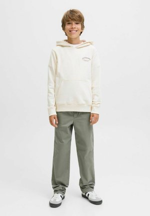 Hoodie crème clair avec une poche avant, intérieur beige et logo discret. Associé à un pantalon baggy vert et des baskets noir et blanc.