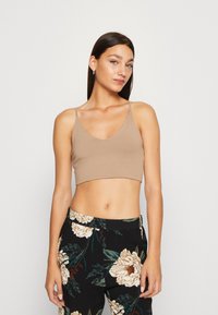 Ljusbrun kort bralette med tunna band, med en mjuk yta och en djup V-ringning, tillsammans med svarta blommiga byxor.