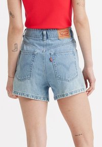 Svijetloplave traper kratke hlače s visokim strukom, izrezanim rubom i klasičnim Levi's stražnjim džepovima. Ima oznaku straga s detaljima brendiranja.