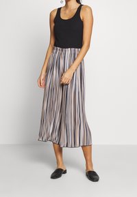 Top in maglia nera a costine abbinato a una gonna plissè con strisce verticali in beige, blu navy e rosa. Scarpe nere in stile slip-on completano il look.