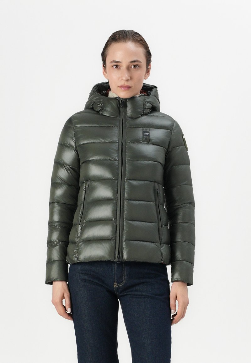Doudoune verte avec capuche, présentant un design matelassé, une texture lisse et une fermeture éclair à l'avant, complétée par des poches latérales et un détail de logo.