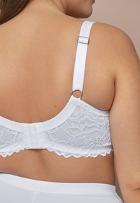Weißes Spitzen-Bralette mit einem glatten, satinähnlichen Band. Verfügt über verstellbare Träger und einen Haken- und Ösenverschluss, akzentuiert durch eine gewellten Spitzenkante.