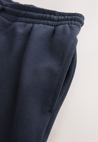 Donkerblauwe joggingbroek met een elastische tailleband, zijzak en gestructureerde stof. Heeft een slanke, op maat gemaakte pasvorm en nette naden.