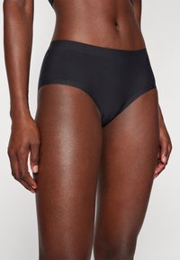 Close-up of a person wearing seamless black underwear, showing torso, hips, and upper thighs against a plain background.