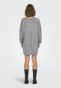 Robe tricotée oversized grise avec de longues manches, un col rond et un ourlet côtelé. Assortie avec des bottes noires jusqu'aux genoux.