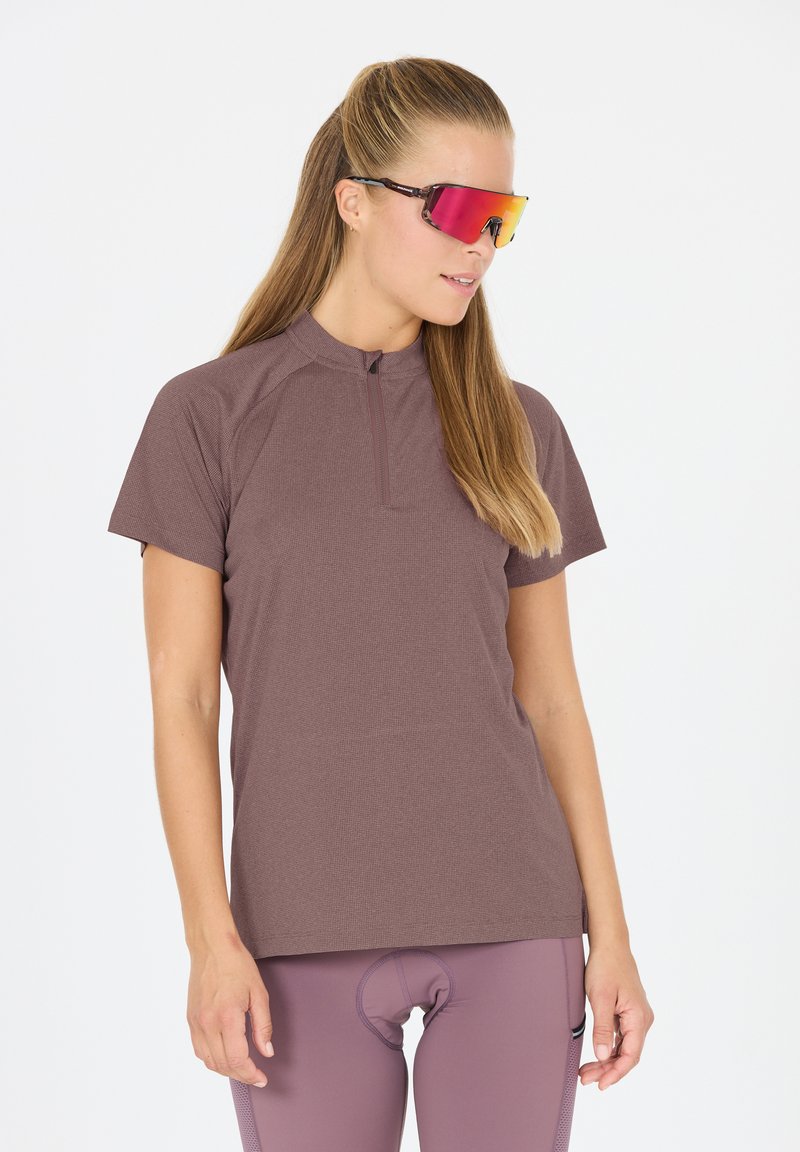 Maillot de cyclisme à manches courtes, de couleur brun clair, avec un col zippé, en tissu texturé, associé à des lunettes de soleil teintées de rose et à des leggings assortis.