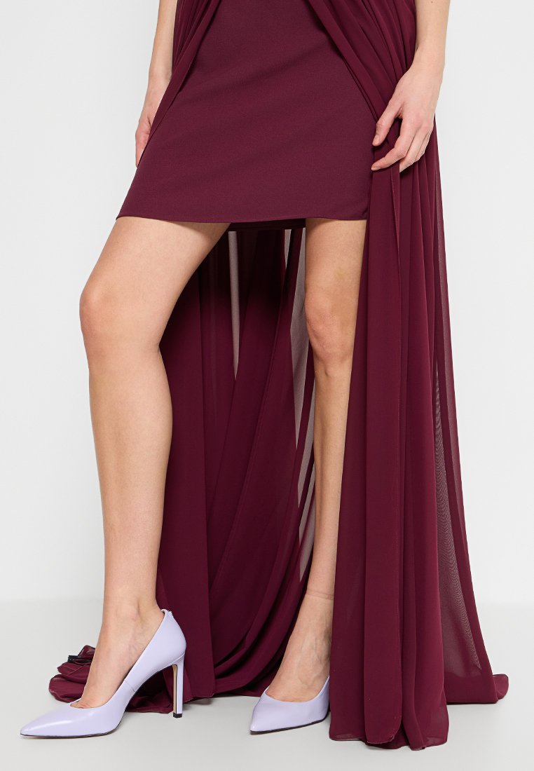Helle lila High-Heels mit einer spitzen Schuhspitze. Glatte Textur, glänzende Oberfläche, getragen zu einem maroonen Kleid mit fließendem Stoff.