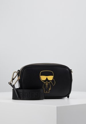 Black synthetic crossbody bag with a gold cartoon character graphic, zipper closure, and a detachable black strap featuring embossed text.