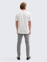 T-shirt branca de algodão com decote redondo, combinada com calças slim fit cinza claro. O conjunto é completado com sapatilhas pretas.