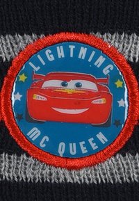 Knitted beanie featuring a round, embroidered patch with a red car character, blue background, and text "LIGHTNING MC QUEEN" in white letters.