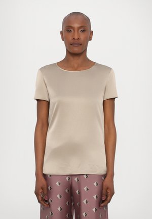 Kortermet beige topp laget av glatt stoff med rund hals; kombinert med mønstrede rosa bukser som har diamantskformer i mørke farger.