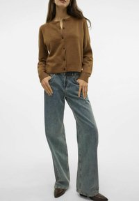 Brun ullblandning kofta med rund halsringning, framknappar och ribbade ärmslut, i kombination med ljusblå vida jeans och spetsiga bruna skor.