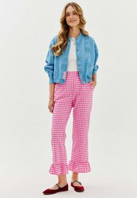 Světle modrá bomber bunda s jemným vzorem, bílý top, kalhoty s růžovým kostkovaným vzorem a volánky na lemech, a červené baleríny se šedými akcenty.