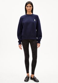 Navy blue sweatshirt with a small white ribbon logo, paired with black leggings featuring a textured zebra pattern, and black slip-on shoes.