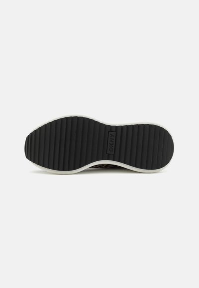 Semelle en caoutchouc noir avec des rainures horizontales et un accent de semelle intermédiaire blanche. Logo DKNY en relief sur le côté. Détail de grip texturé et robuste.