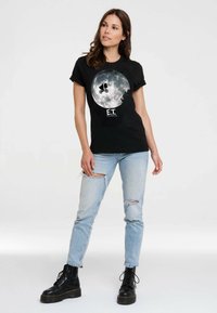 Black cotton t-shirt featuring a large graphic of a bicycle silhouette against a full moon, with "E.T." printed below. Worn with light blue distressed jeans and black lace-up boots.