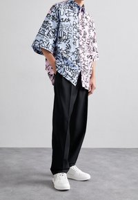 Camisa de manga corta en azul claro y rosa con un audaz texto en negro estilo graffiti. Un pantalón negro de pierna ancha y unas zapatillas blancas complementan el atuendo.