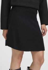 Zwarte gebreide rok met een zachte textuur, voorzien van een aansluitende tailleband en een asymmetrische zoom. Geschikt voor verschillende informele gelegenheden.