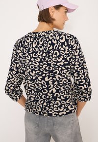 Maglia navy con stampa leopardata crema, maniche lunghe e scollatura rotonda. Abbinata a jeans grigi chiari, per un look casual.