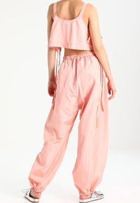 Roze cropped top met verstelbare schouderbanden, gecombineerd met losse roze broeken met een elastische tailleband en aantrekkoorden aan de zijkanten.