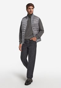 Szara pikowana kamizelka na szarym swetrze, w połączeniu z ciemnymi dżinsami i czarnymi butami wsuwanymi. Gładka tekstura z poziomym wzorem pikowania.