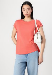 Koral kortermet t-skjorte laget av mykt stoff, sammen med lyseblå denimjeans. En liten hvit håndveske med gullfarge detaljer.