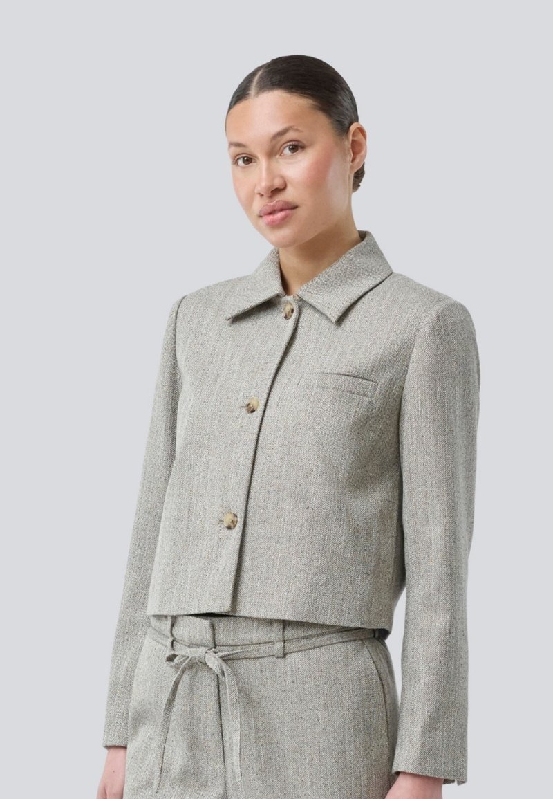Gekürzte grau melierte Jacke mit spitzem Kragen, Knopfschluss und Brusttasche. Leichte Textur und maßgeschneidertes Design ergänzen die passende Hose.