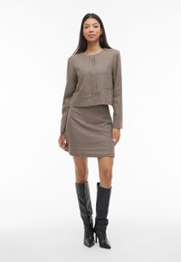 Dvoslojni komplet s uzorkom u smeđim i bež kockicama, sastavljen od uskog kratkog topa s dugim rukavima i pripijene mini suknje, upareno s visokim crnim čizmama.