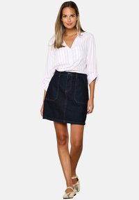 Denim skirt with front pockets, paired with a white shirt featuring pink stripes. The model wears light-colored shoes and stands upright.