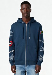 Sweat à capuche zippé marine en mélange de coton avec poches avant. Comprend des impressions graphiques blanches et des accents colorés sur les manches. Capuche ajustable avec cordon de serrage.