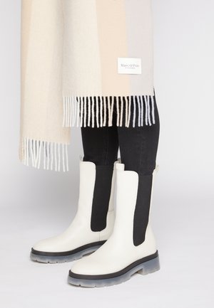 Bottines blanches avec des panneaux latéraux noirs, semelles en caoutchouc, et un design épuré ; associées à une écharpe légère à rayures avec des bords frangés.