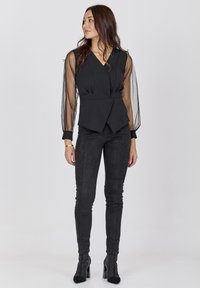 Sort peplum top med gennemsigtige lange ærmer og dyb V-udskæring, parret med sorte skinny bukser og højhælede ankelstøvler.