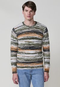 Gebreide trui in meerkleurige strepen: groen, oranje, zwart, wit. Ronde hals, lange mouwen, textuurstof met een zachte afwerking.