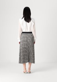 Chemisier blanc avec une jupe plissée à motifs noir et blanc ; taille haute noire ajustée ; talons blancs à lanières ; textures lisses.