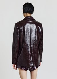 Burgunderfarbene Lederblazer mit glänzender Oberfläche, strukturierten Schultern und einer einzigen Rückennaht, kombiniert mit Pailletten-Shorts.