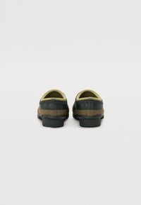 Scarpe slip-on verdi e marroni con un'esterno liscio, retro arrotondato e suola texturizzata; presentano un interno giallo a contrasto.