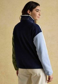 Bavlnená bunda s vysokým golierom, viacfarebnými panelmi v námorníckej modrej, zelenej a svetlomodrej farbe, s výšivkou 'Coules' na chrbte.