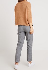 Beige gestrickter Pullover mit fallenden Schultern, kombiniert mit grauen Karohosen und weißen Sneakern, von hinten aufgenommen.