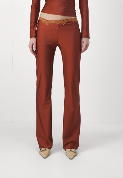 Pantaloni marroni aderenti con una cintura larga e dettaglio in pizzo. Tessuto liscio e elastico con un design a gamba dritta. Accentuati da scarpe beige a punta.