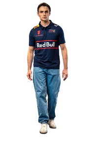 Granatowa koszulka polo z logo Red Bull i czerwonymi akcentami, połączona z jasnoniebieskimi dżinsami i beżowymi trampkami, z krótkimi rękawami i kołnierzykiem.