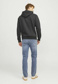 Sudadera con capucha negra y jeans azul. La sudadera tiene un corte holgado con puños y dobladillo acanalados. Los jeans presentan un corte clásico y un lavado desgastado.