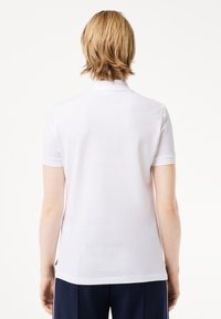 Kurzarm-Poloshirt in Weiß, aus glattem Stoff. Mit Kragen und subtiler Textur, geradem Saum und seitlichen Schlitzen.