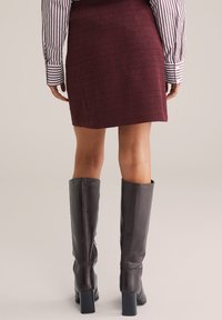 Mini falda de tweed burdeos con un acabado texturizado, combinada con botas de cuero marrón oscuro hasta la rodilla con tacones gruesos.