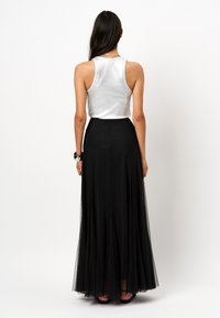 Zwarte maxi rok met een vloeiende uitstraling, gemaakt van tule, gecombineerd met een aansluitend zilver metallic tanktop, die een gladde textuur en gelaagd uiterlijk toont.