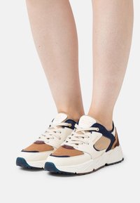 Sneaker mit cremefarbenen, marineblauen, braunen und tanfarbigen Wildleder- und Leder-Panels. Weiße Schnürsenkel, strukturierte blaue Außensohle und Branding auf der Zunge.