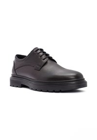 Chaussure en cuir noire à lacets avec semelle épaisse en caoutchouc et bout arrondi, inclinée pour montrer le côté extérieur et l'avant sur fond blanc.