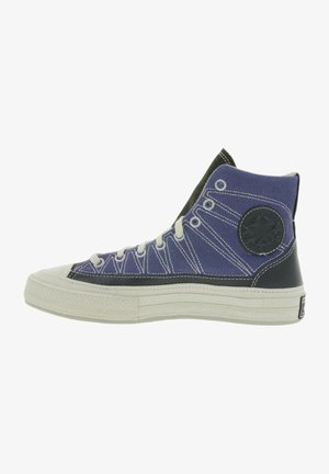 High-top sneaker with a blue canvas upper, white stitching, black leather accents, round logo patch, and textured white rubber sole.